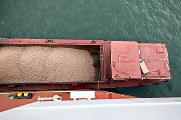 Loading bulk cargo of limestone from barges into a bulk carrier by using ship cranes and grabs at...