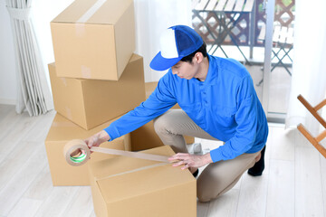 作業服を着た男性が引っ越しの段ボールを梱包するイメージ
