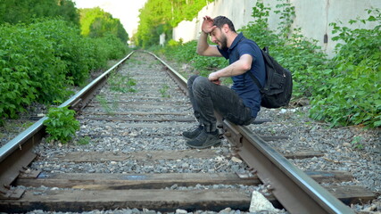 A man with a backpack on his back sat down to rest on the rails. Travel on railroad tracks. Old train track