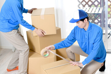 作業服を着た複数の男性が引っ越しの段ボールを梱包するイメージ