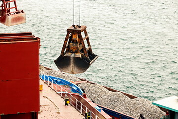 Loading bulk cargo of limestone from barges into a bulk carrier by using ship cranes and grabs at...