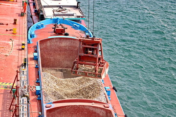 Loading bulk cargo of limestone from barges into a bulk carrier by using ship cranes and grabs at...