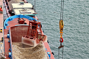 Loading bulk cargo of limestone from barges into a bulk carrier by using ship cranes and grabs at...
