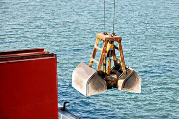 Loading bulk cargo of limestone from barges into a bulk carrier by using ship cranes and grabs at...