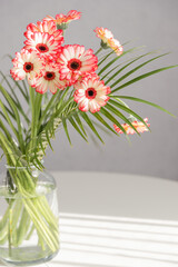 Bouquet of pink gerberas in a glass vase on a white table. Flowers in the interior and as a gift for a holiday. Vertical photo