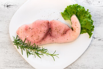 Raw Swordfish fillet covered with black pepper and with rosemary sprigs on white plate.