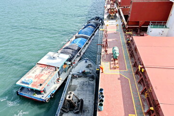 Loading bulk cargo of limestone from barges into a bulk carrier by using ship cranes and grabs at...