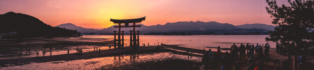 Amazing super wide panorama view of torii gate and sunset with travelers over the sea with...