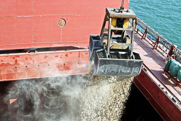 Loading bulk cargo of limestone from barges into a bulk carrier by using ship cranes and grabs at...