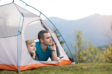 Young father and his child son hiking together in summer mountains. Active family resting in tourist tent.