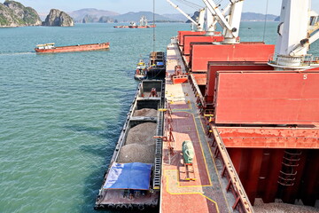 Loading bulk cargo of limestone from barges into a bulk carrier by using ship cranes and grabs at...