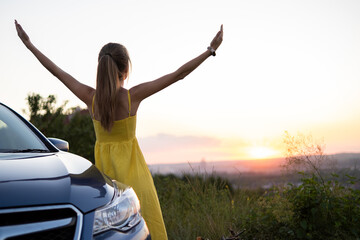 Carefree woman driver in yellow summer dress enjoying warm evening near her car. Travel and vacation concept.
