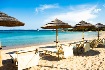 (Selective focus) Stunning view of some thatch umbrellas and sun chairs on a beach bathed by a beautiful, turquoise sea. Sardinia, Italy.