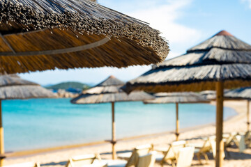 (Selective focus) Stunning view of a thatch umbrella in the foreground and blurred sun chairs on a...