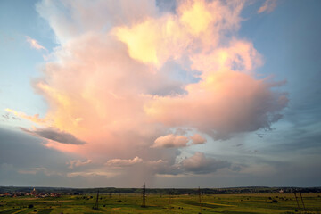 Dramatic stormy sunset over rural area with puffy clouds lit by orange setting sun and blue sky.