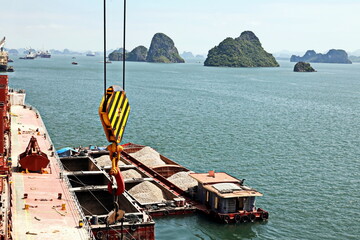 Loading bulk cargo of limestone from barges into a bulk carrier by using ship cranes and grabs at...
