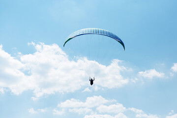 Blue Paraglider flying into the sky with clouds on a sunny day