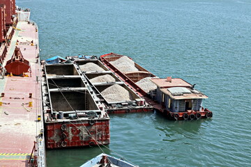 Loading bulk cargo of limestone from barges into a bulk carrier by using ship cranes and grabs at...