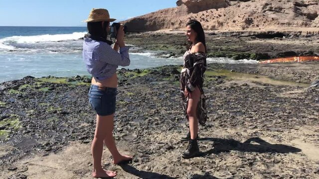 A photographer is taking pictures of a girl posing on the beach, it's summer and the day is beautiful. Two girls at the beach