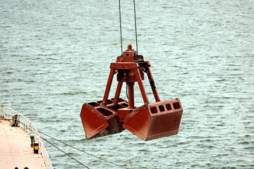 Loading bulk cargo of limestone from barges into a bulk carrier by using ship cranes and grabs at...