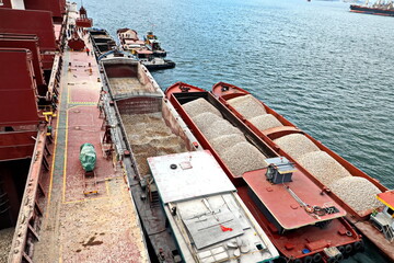 Loading bulk cargo of limestone from barges into a bulk carrier by using ship cranes and grabs at...