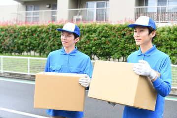屋外で作業服を着た複数の男性が引っ越しの段ボールを運ぶイメージ
