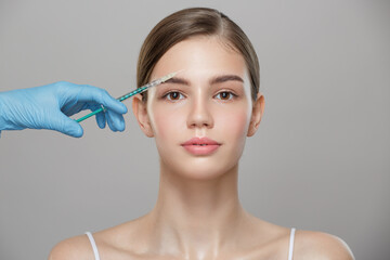 People, cosmetology, plastic surgery and beauty concept - surgeon or beautician hand holding a syringe near woman face over gray background.