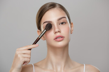 Obraz premium Portrait of a girl with perfect skin holding a makeup brush. Gray background.