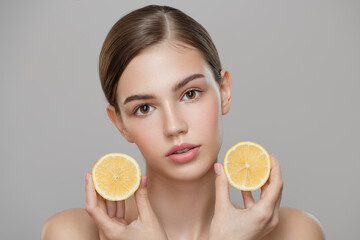 Organic cosmetics concept. A young girl with clean skin holds lemon slices near her face. Gray background.