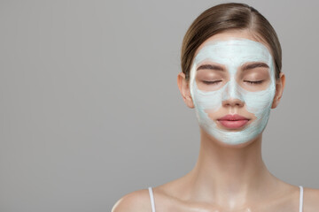 Portrait of beautiful woman with blue cream mask on her face. Skin care concept. Gray background.