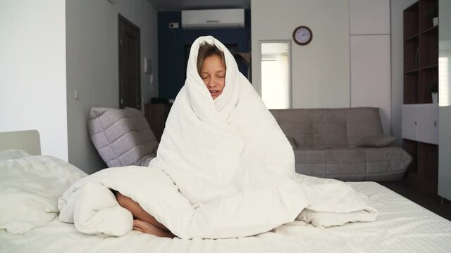 Symptoms of coronavirus. A sick young woman, feeling cold fever, freezes without central heating, feeling cold at home. Covered with a warm white blanket. Shivering, sitting on the couch, stressed out