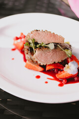 Duck meat in red berry sauce with berries, flower, salad and vegetables on a white plate
