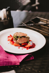 Duck meat in red berry sauce with berries, flower, salad and vegetables on a white plate