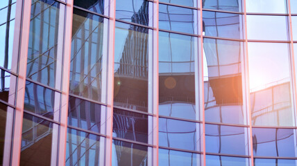Abstract closeup of the glass-clad facade of a modern building covered in reflective plate glass. Architecture abstract background. Glass wall and facade detail.