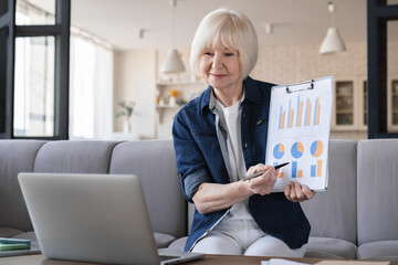 Remote distant job, working from home office. Old elderly senior businesswoman teacher lecturer conducting lectures lessons at home, discussing charts and tables with her colleagues and clients