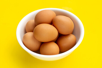 Fresh eggs in white bowl on yellow background.