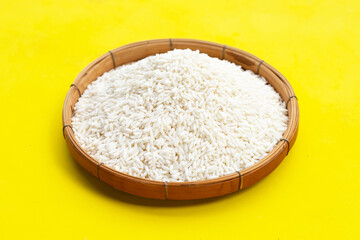 Raw sticky rice in bamboo basket on yellow background.