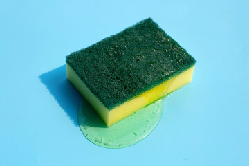 Kitchen sponge with dish washing liquid on blue background.