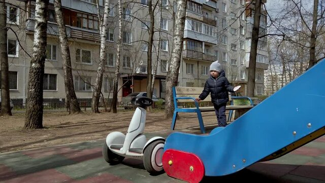 little boy funny playing on the playground with the help of new technology segway gadget in early spring