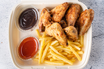 Fried chicken wings with french fries potato chips in portion for delivery pick up lunch close up...