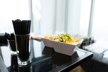 Glass of Black Straws on Bar Top with Lemons and Limes