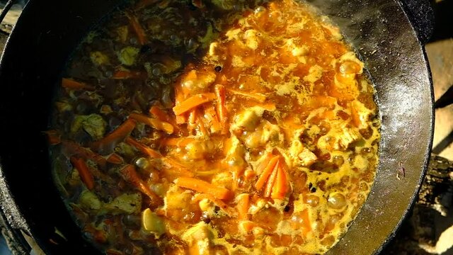 Cooking the Uzbek national dish - pilaf. Cast iron cauldron on a stand. Fire from wood firewood. The basis of plovazirvak. Zirvak from meat. onions, carrots, cumin, turmeric, oil, frying. Grinding wit