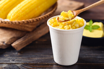Sweetcorn with butter in a biodegradable cup eating by spoon on wooden background
