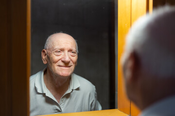Old man looking happy and smiling at his reflection in front of a mirror in the bathroom