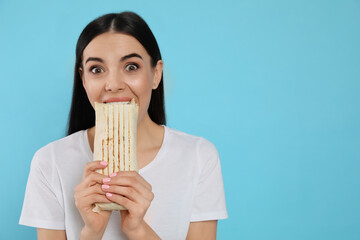 Young woman eating delicious shawarma on light blue background. Space for text