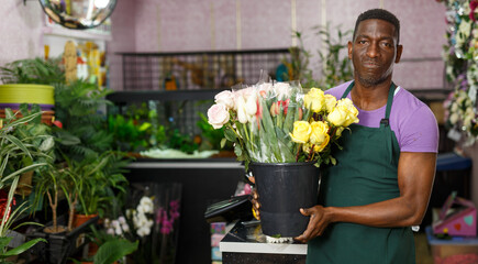 Smiling African-American man florist standing with fresh flowers in his floral shop