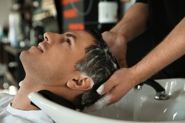 Professional barber washing client's hair at sink in salon, closeup