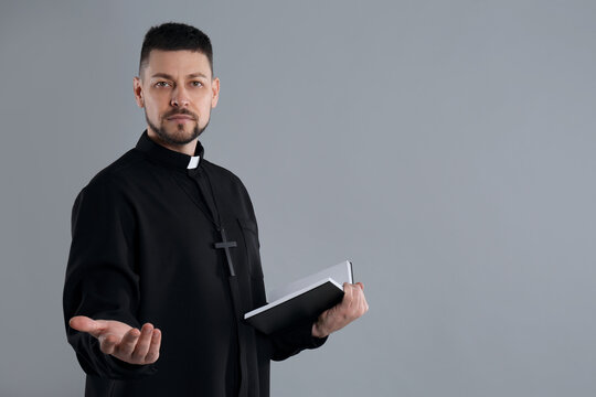 Priest with Bible praying on grey background, space for text