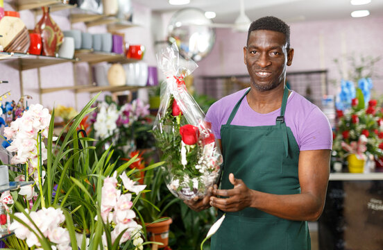 Positive African American male florist offering flower arrangements at his flower shop