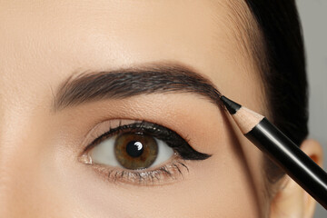 Naklejka premium Young woman correcting eyebrow shape with pencil, closeup view